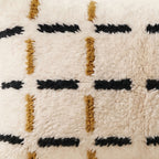 Side view of the Tazart Moroccan pillow showing its ivory, black and mustard wool pile