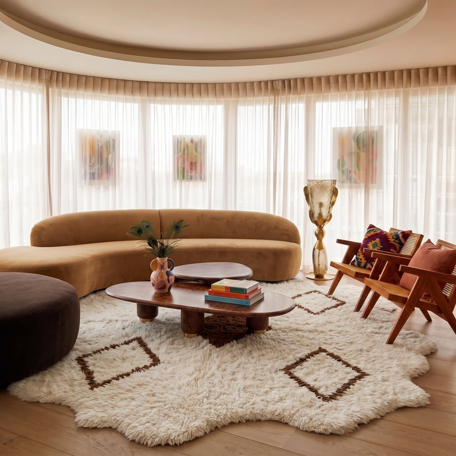 Ivory and brown Beni Ourain rug positioned in living room with curved sofa and wooden furniture