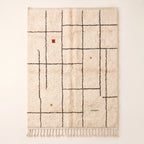 Ivory Beni Ourain rug with charcoal grid lines and scattered rust, ochre and sage accents, flat lay on white background
