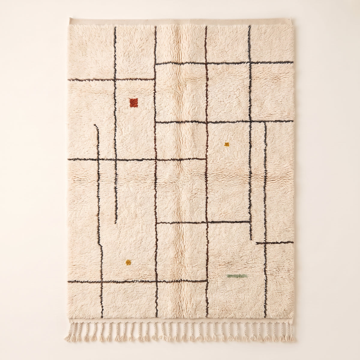 Ivory Beni Ourain rug with charcoal grid lines and scattered rust, ochre and sage accents, flat lay on white background