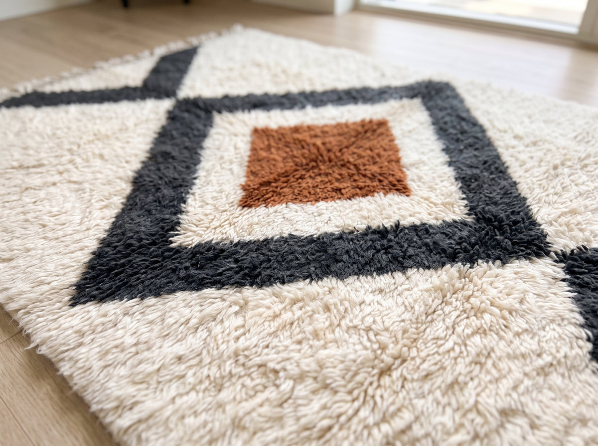 Angled detail shot of charcoal diamond border and terracotta center on ivory ground, showing handwoven texture