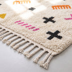 Detail of hand-knotted fringe and symbols at rug edge, showing orange comb motif, magenta dash pattern and black cross on ivory ground