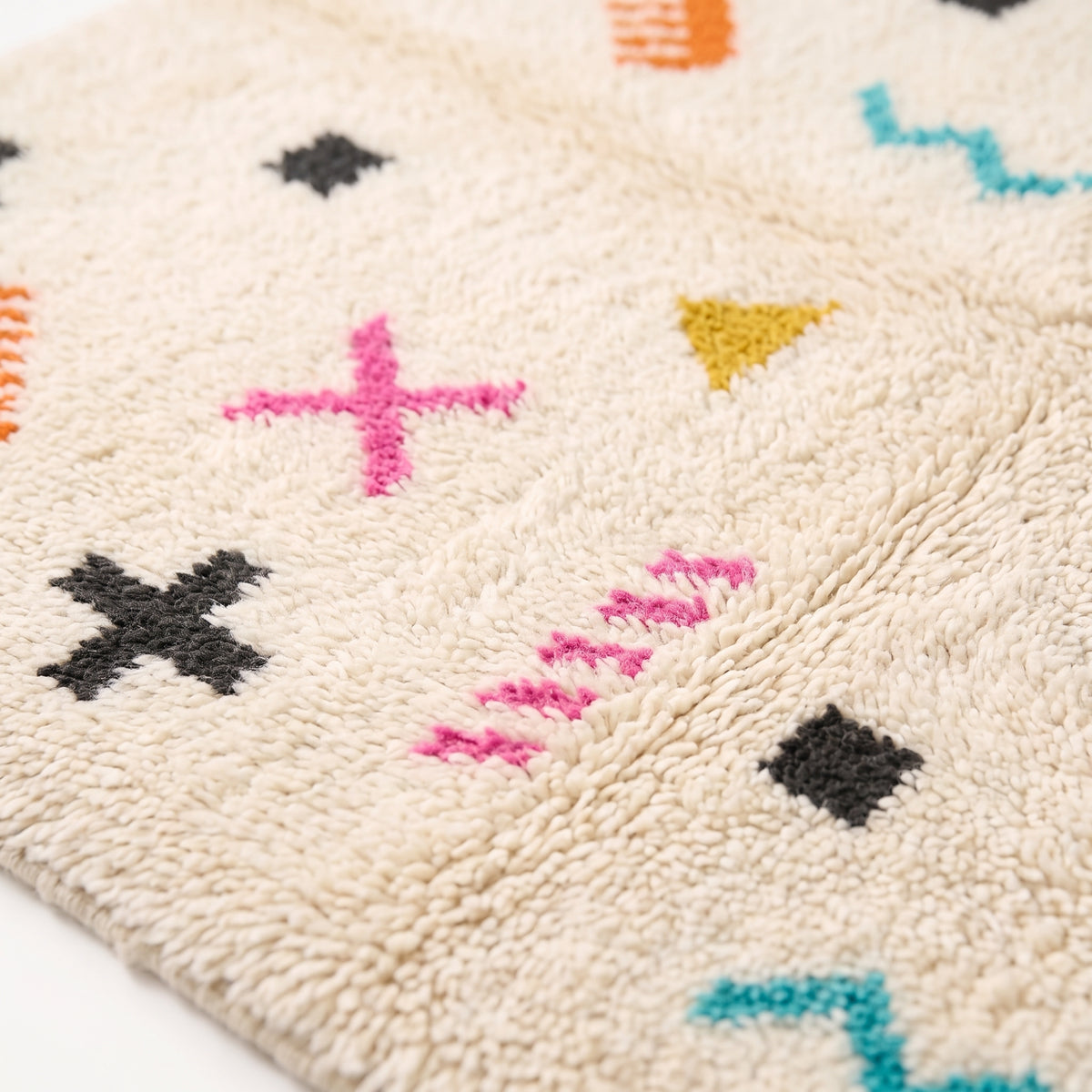 Close-up detail of soft handwoven pile showing magenta X mark, gold triangle, teal zigzag and black dashes on ivory wool
