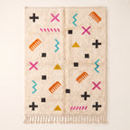 Ivory Azilal rug with scattered magenta, teal, orange, black and gold symbols including crosses, X marks, zigzags, triangles and combs on a cream ground, flat lay