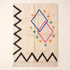 Ivory Azilal rug with navy and pink diamond outlines, orange and green plus-sign crosses, and black zigzag border motif, full flat view