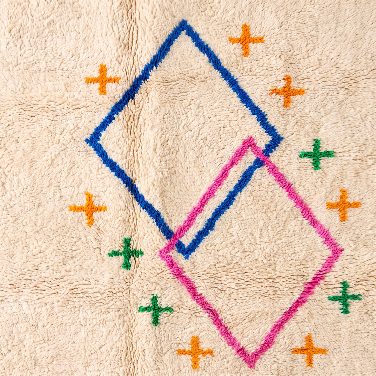 Close-up of diamond and cross motif showing hand-knotted navy, pink, orange, and green on ivory wool