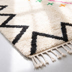 Corner of Azilal rug showing black zigzag border and cream-colored hand-tied fringe
