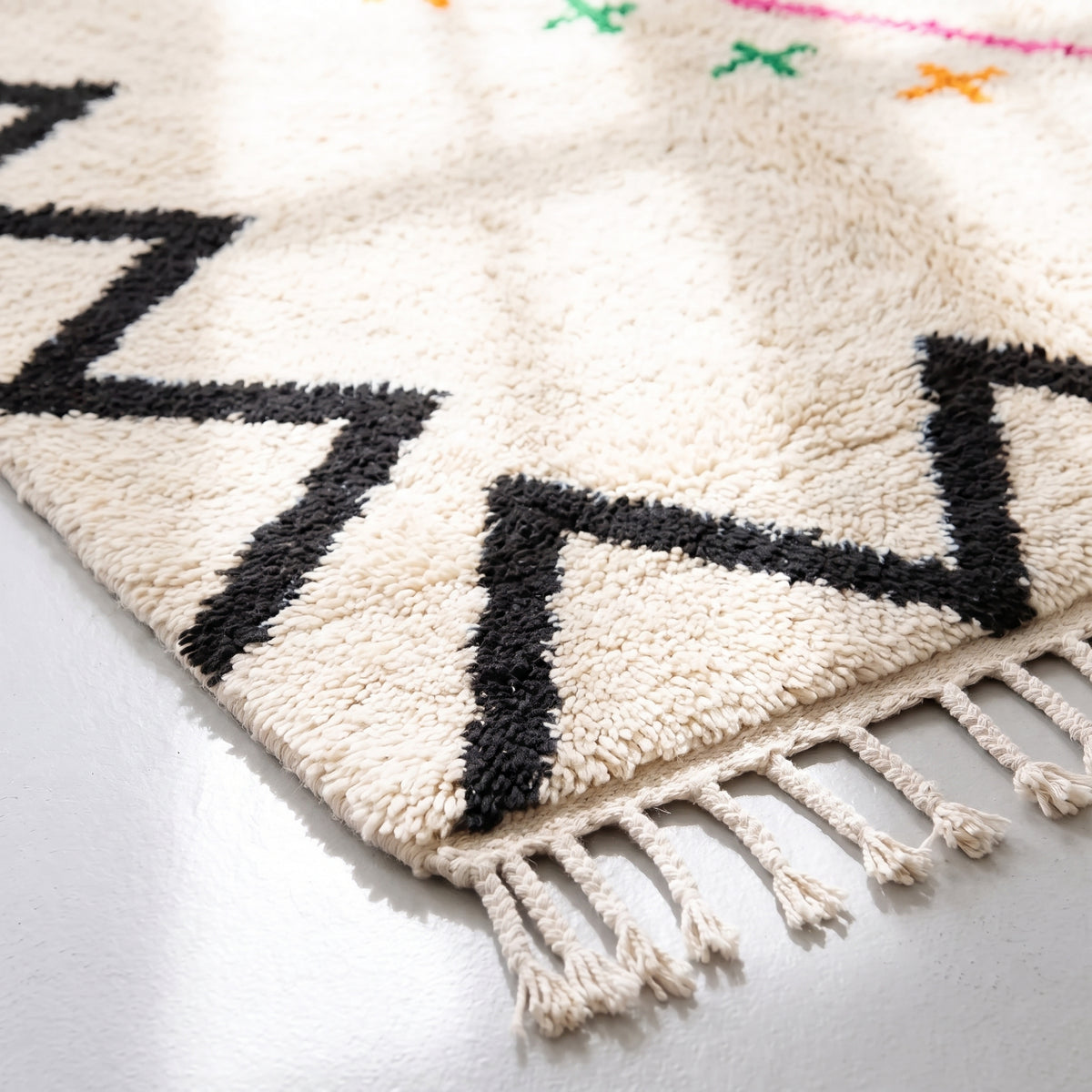 Corner of Azilal rug showing black zigzag border and cream-colored hand-tied fringe