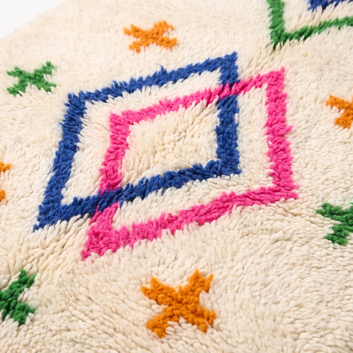 Close-up of hand-knotted pile showing navy, pink, and orange diamond and cross motifs on ivory wool