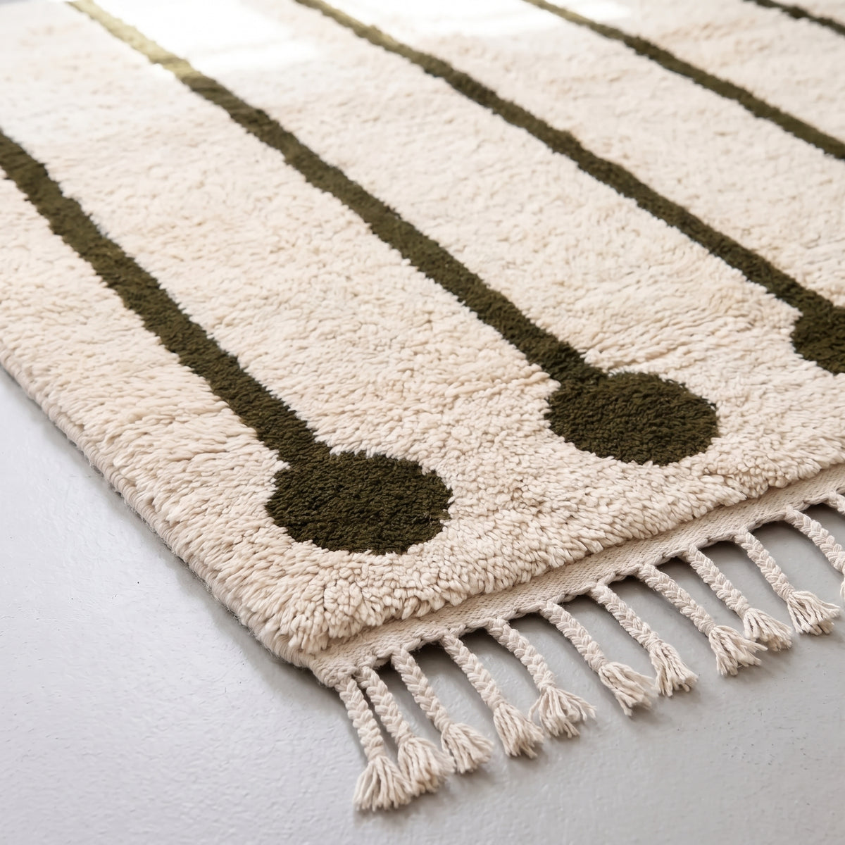 Detail of ivory Beni Ourain rug fringe and lower edge showing olive lollipop motif and cream wool fringe