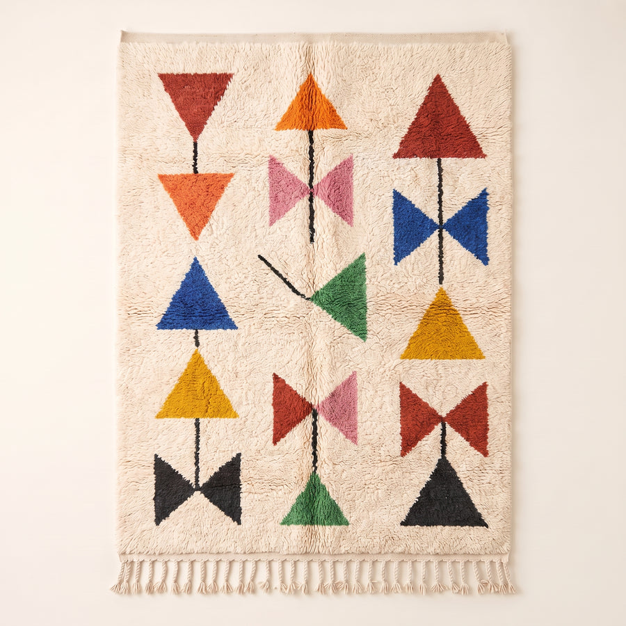 Ivory Azilal rug with coloured triangles and bows in red, orange, navy, pink, green, gold and black, flat lay on plain background
