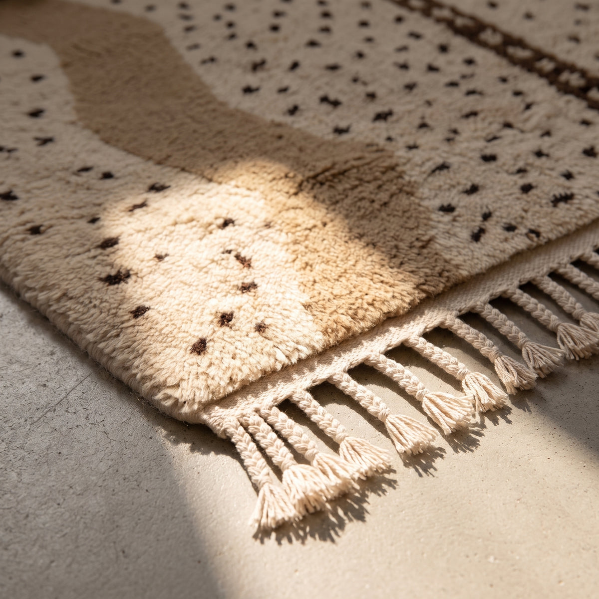 Corner detail of Beni Ourain rug showing cream wool fringe and black diamond motifs at edge