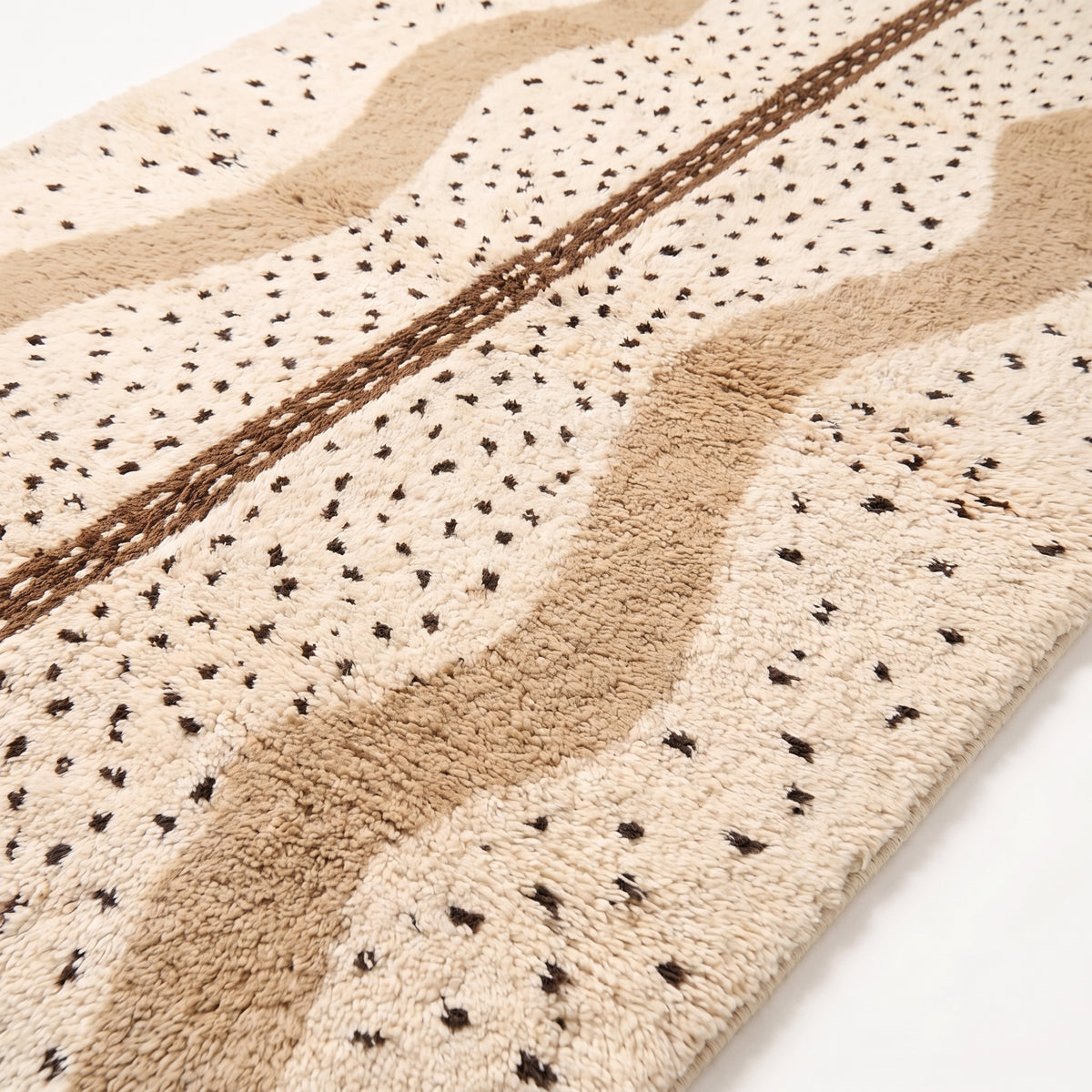 Close-up of Beni Ourain weave showing scattered black diamonds, tan and ivory wool pile with brown center band detail