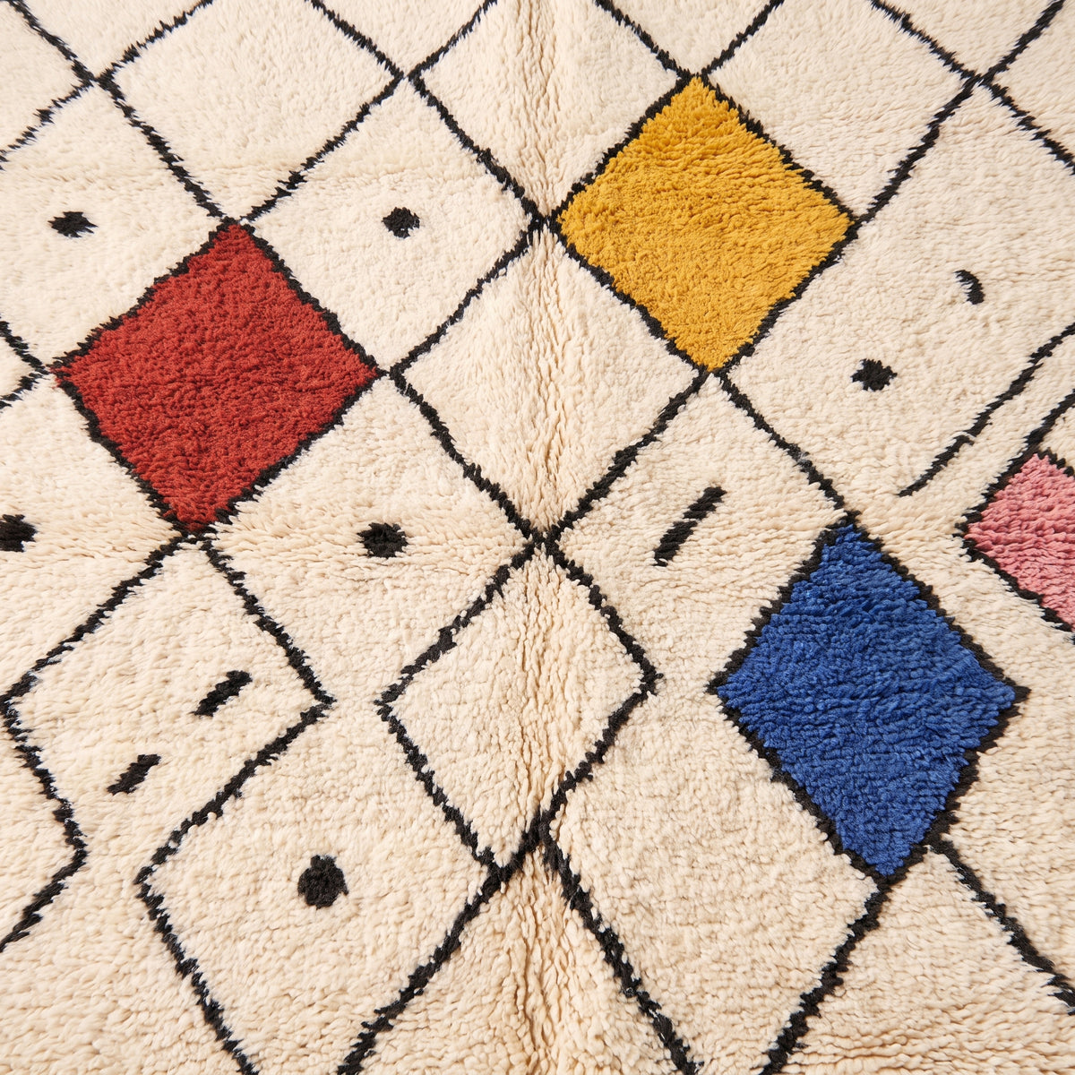 Close-up of Tiziri rug showing dyed wool diamond blocks in terracotta, gold and navy against ivory pile with black scatter marks