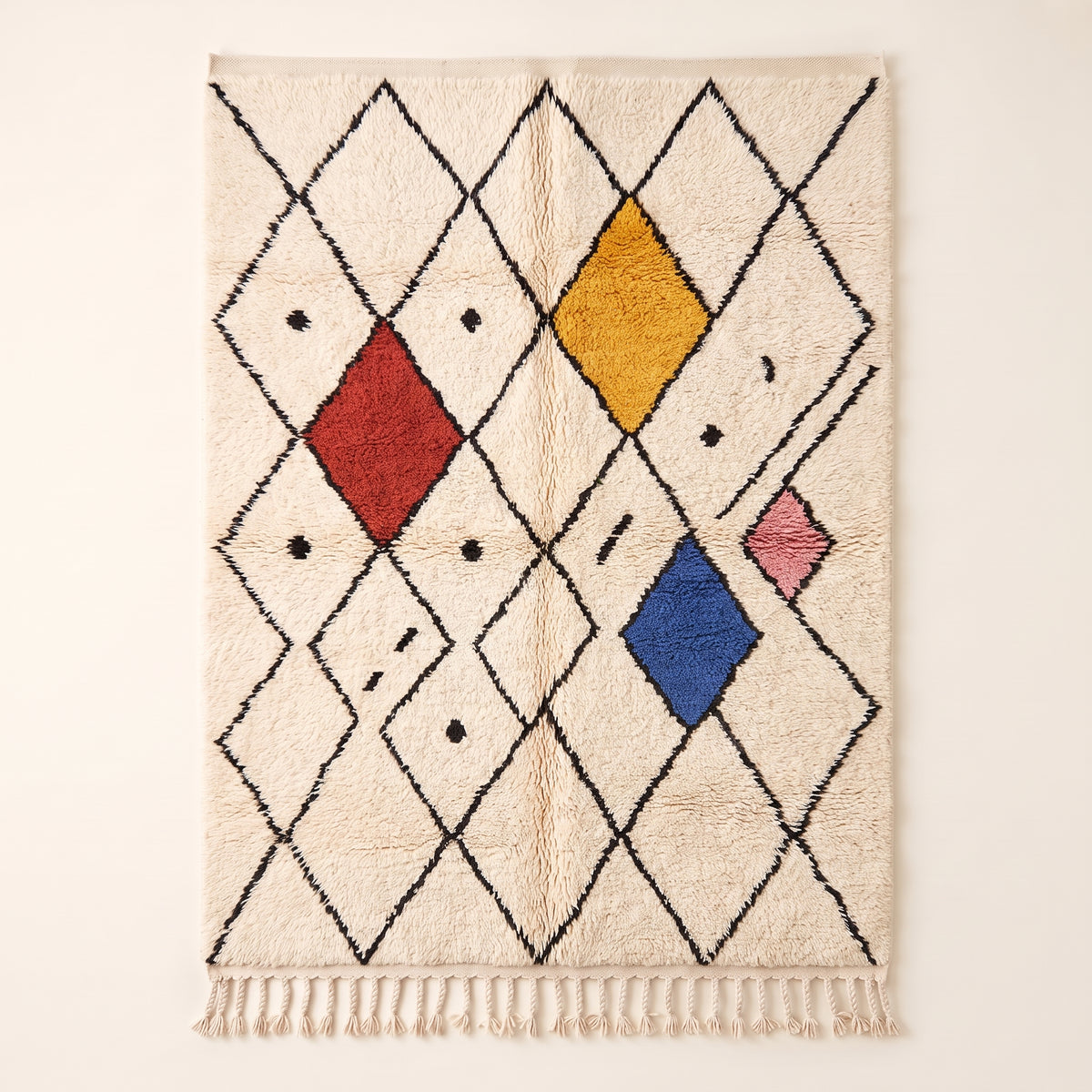 Ivory Beni Ourain rug with dark brown diamond lattice, terracotta, gold, navy and blush wool diamonds scattered throughout, small black accent marks, fringe detail at bottom