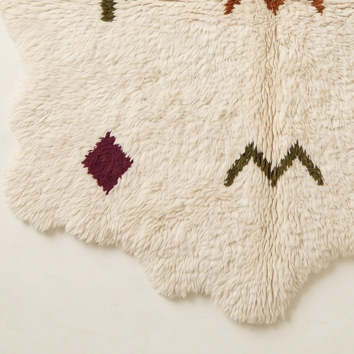 Corner and edge detail showing wavy irregular fringe and burgundy diamond symbol near rug edge