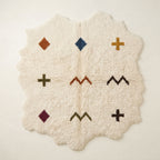 Ivory Beni Ourain rug with irregular wavy edges, scattered with terracotta diamond, navy diamond, gold cross, olive cross, rust chevrons, burgundy diamond, and dark olive chevron and dark cross motifs