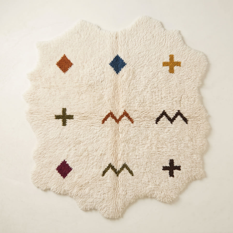 Ivory Beni Ourain rug with irregular wavy edges, scattered with terracotta diamond, navy diamond, gold cross, olive cross, rust chevrons, burgundy diamond, and dark olive chevron and dark cross motifs