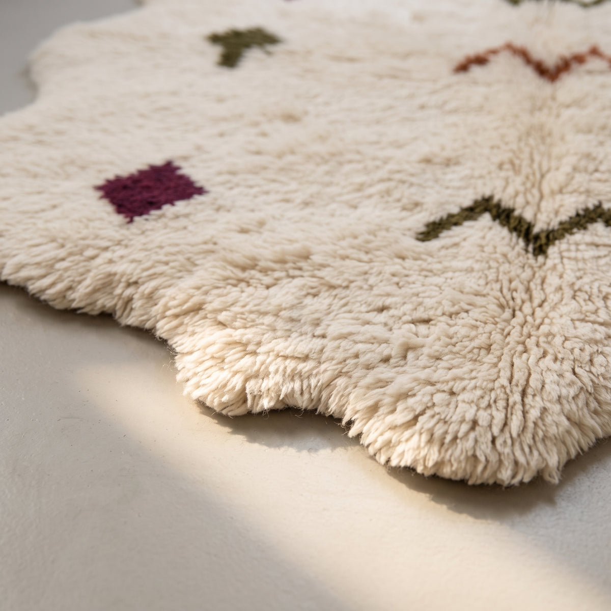 Angled pile detail revealing burgundy diamond and olive chevron symbols in soft Beni Ourain wool