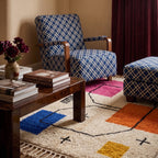 Magenta, orange, blue and gold Azilal rug styled in living room with wooden furniture and blue patterned chair