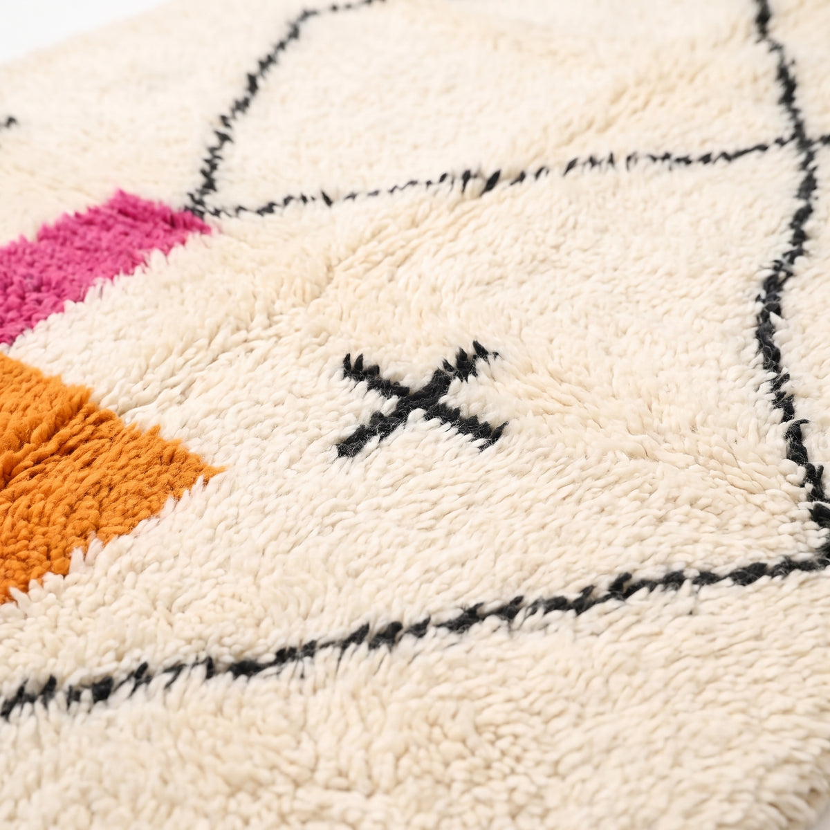 Close-up of Azilal rug pile showing magenta, orange and ivory wool texture with black line detail