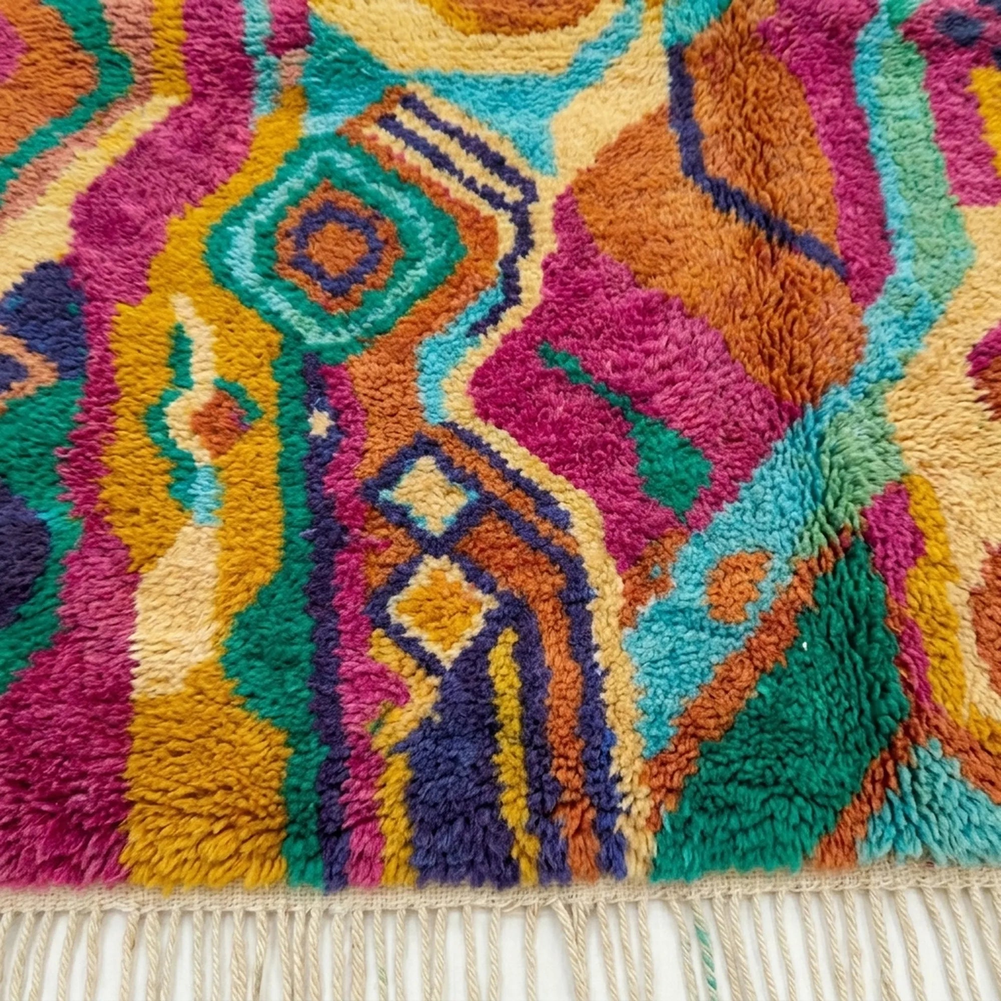 Lower-edge view of Awrmas showing layered teal, orange, magenta and cream bands beside the fringe
