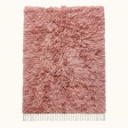 Flat lay of mauve Beni Ourain rug with dense pile and ivory fringe on plain background