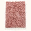 Flat lay of mauve Beni Ourain rug with dense pile and ivory fringe on plain background