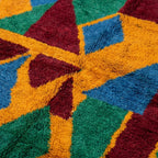 Fringe and edge detail of the Imazigh Boujaad rug beside bold green, mustard and burgundy geometric shapes