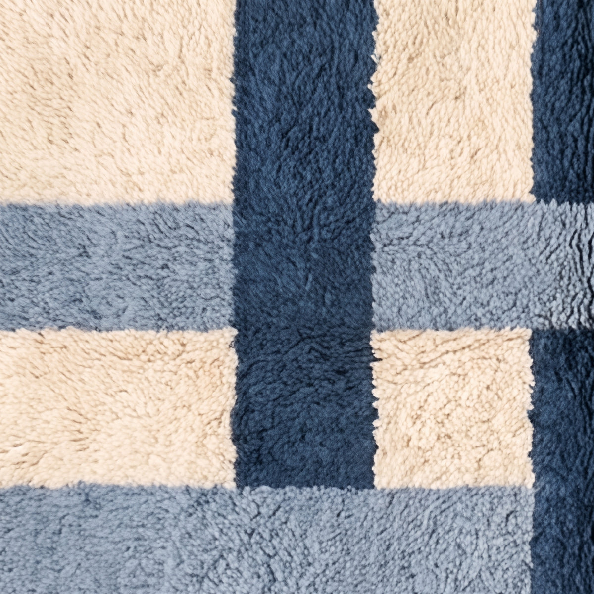Macro detail of cross grid pattern showing color blocks and hand-knotted texture in navy, slate and cream