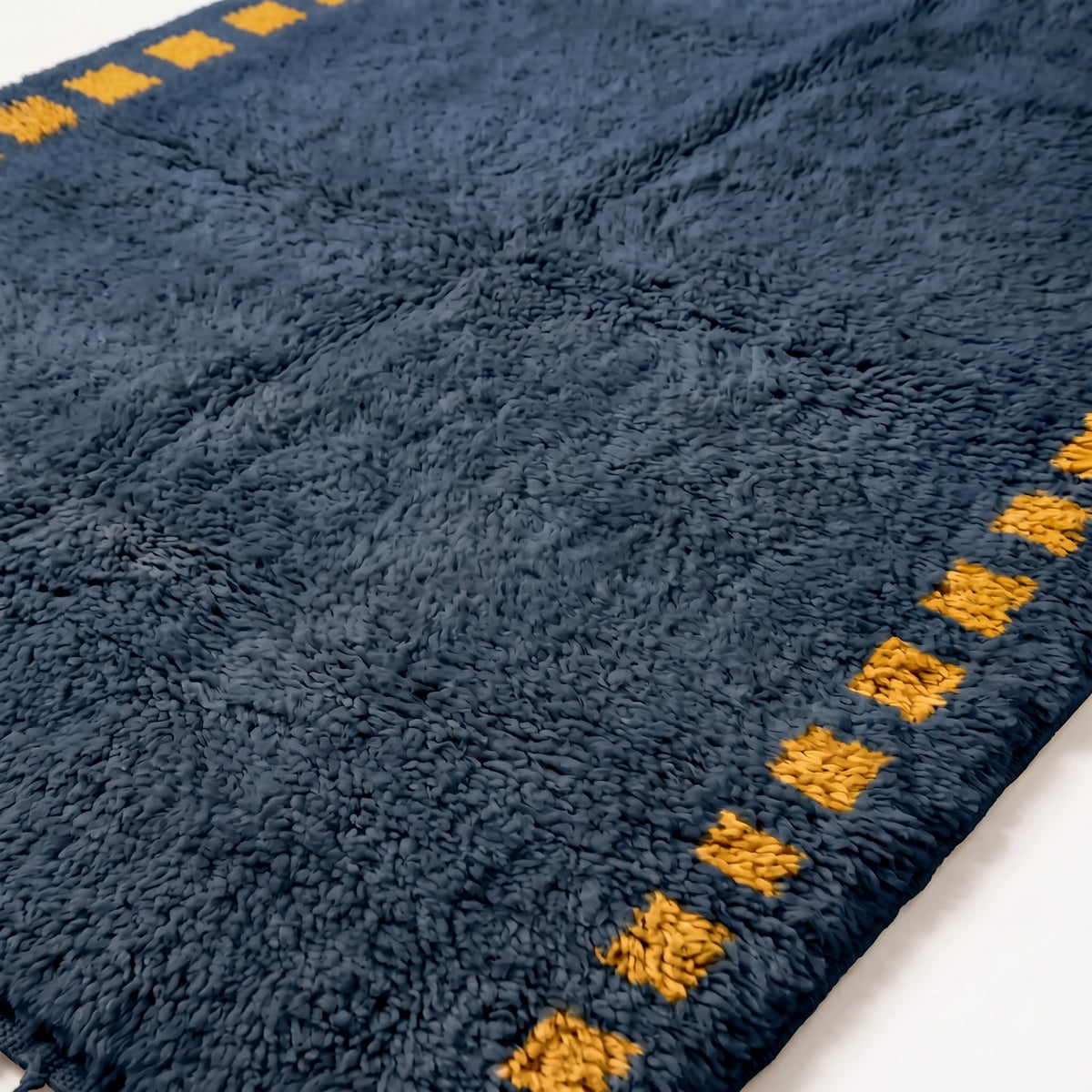 Close-up of dense plush pile texture showing navy wool with saffron square motif detail