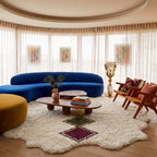 Tafrara rug in modern curved living room with blue sofa, yellow pouf and wooden furniture, showing lozenge chain detail in situ