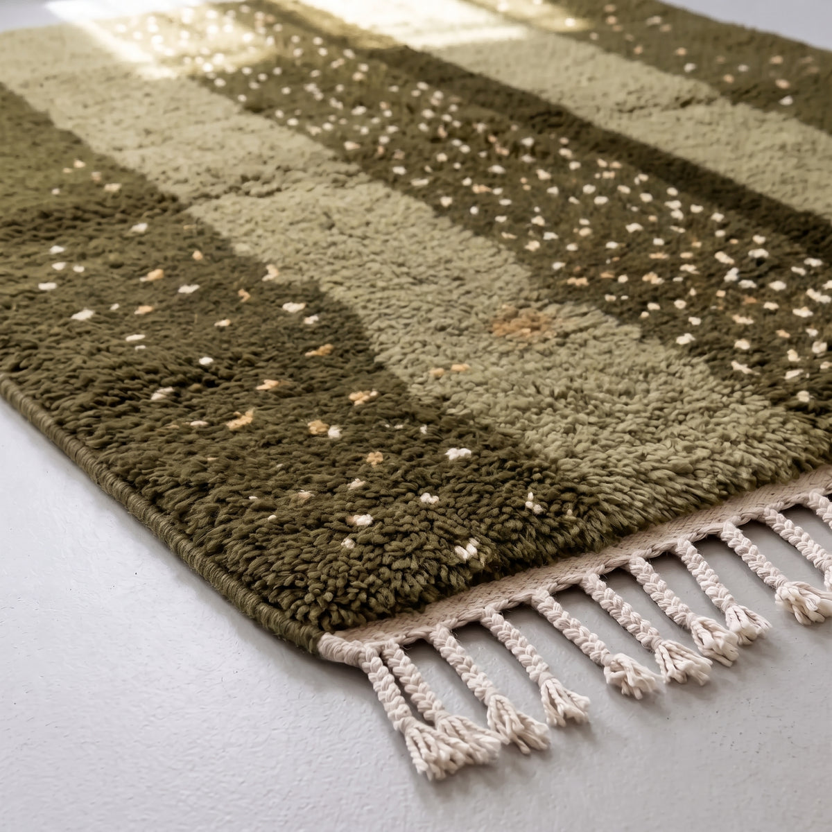 Corner detail of Mrirt rug showing dense dots on dark olive ground and fawn solid band with fringe edge
