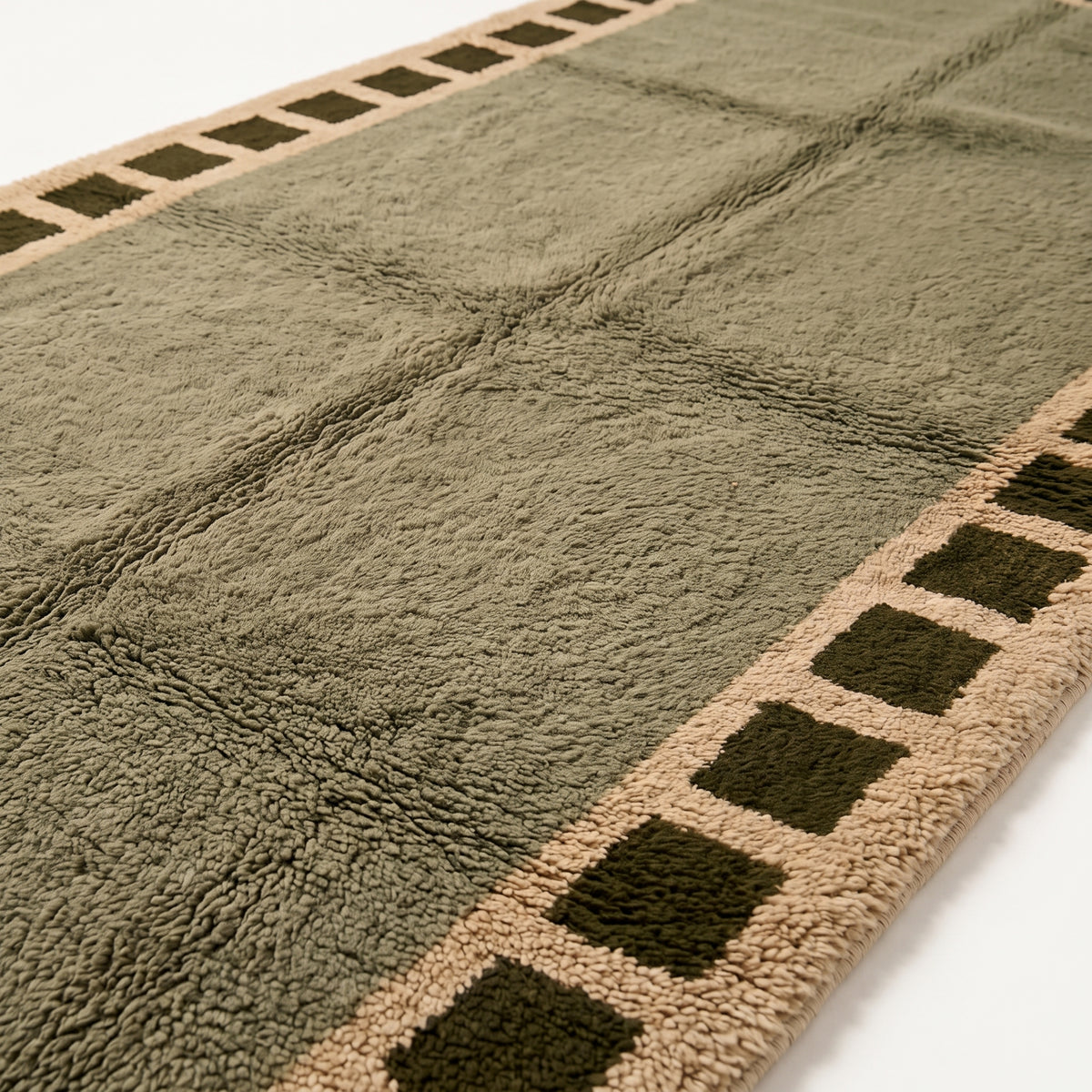 Close-up of olive Mrirt rug pile showing dense texture and checkered border detail