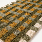 Close-up of plush hand-knotted pile showing olive, mustard, sage and ivory grid blocks