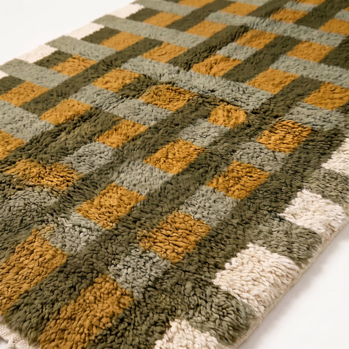 Close-up of plush hand-knotted pile showing olive, mustard, sage and ivory grid blocks