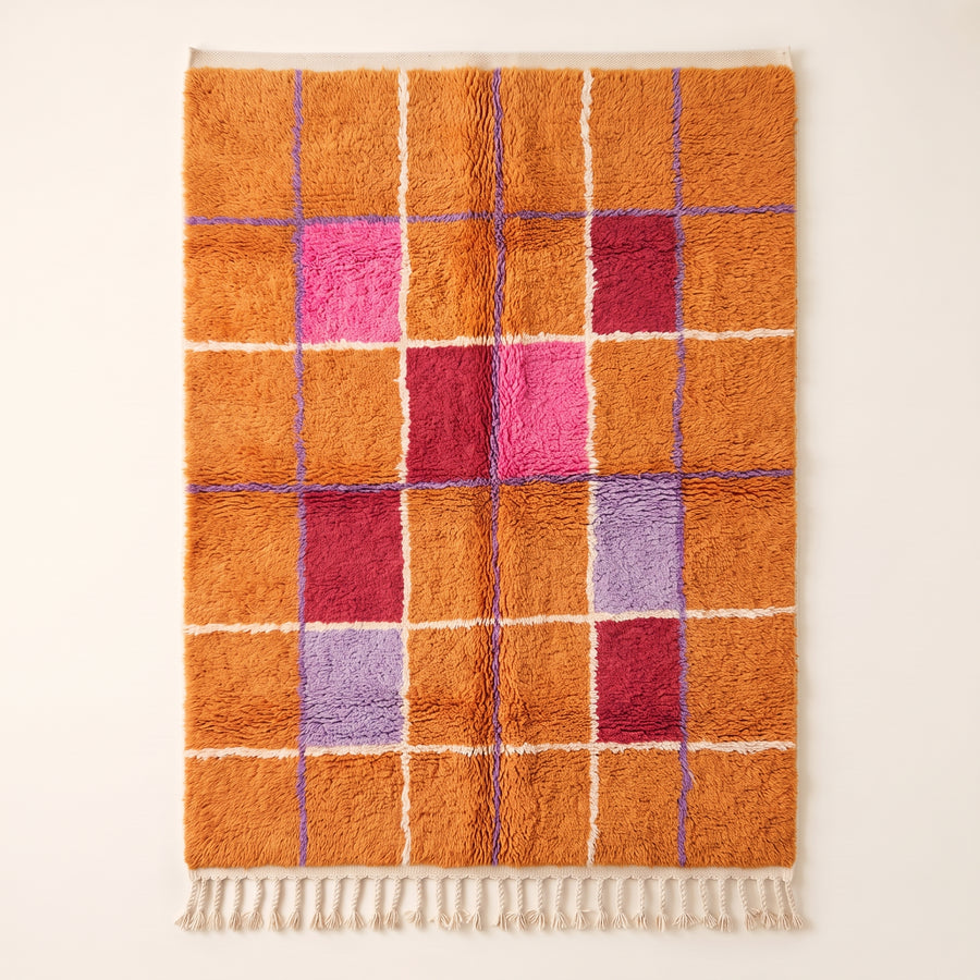 Orange, hot pink, deep red and purple Mrirt rug with geometric window grid pattern separated by white and periwinkle lines, flat view on plain background with cream fringe