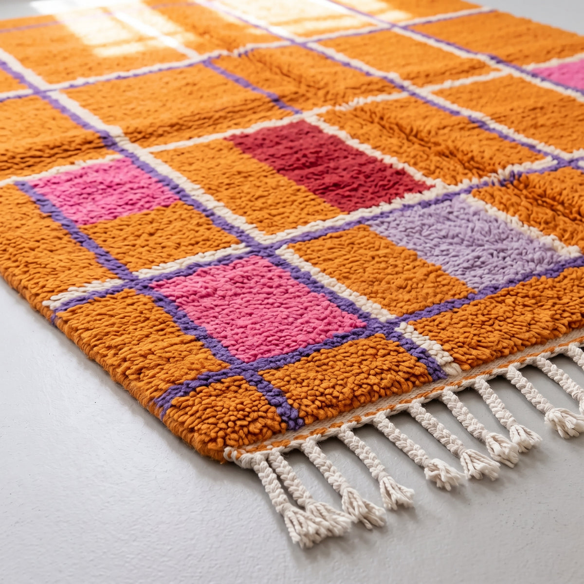 Overhead angled pile detail of the Mrirt rug showing the geometric grid with even knots in orange, pink, red, purple and white sections