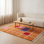 Orange, pink, red and purple geometric grid Mrirt rug laid in front of a cream upholstered sofa with wooden coffee table in a bright, minimalist living room