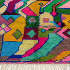 Fringe and edge detail of the Iderfan Boujaad rug beside jagged mustard, teal, pink and green forms