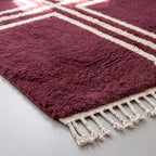 Angled view of plum rug pile showing depth and softness of hand-knotted wool with ivory cross pattern