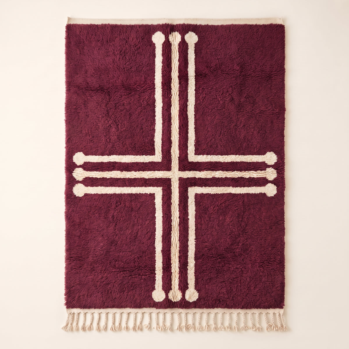 Plum and ivory Beni Ourain rug with bold geometric cross motif and decorative terminals, flat lay on plain background