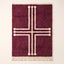 Plum and ivory Beni Ourain rug with bold geometric cross motif and decorative terminals, flat lay on plain background