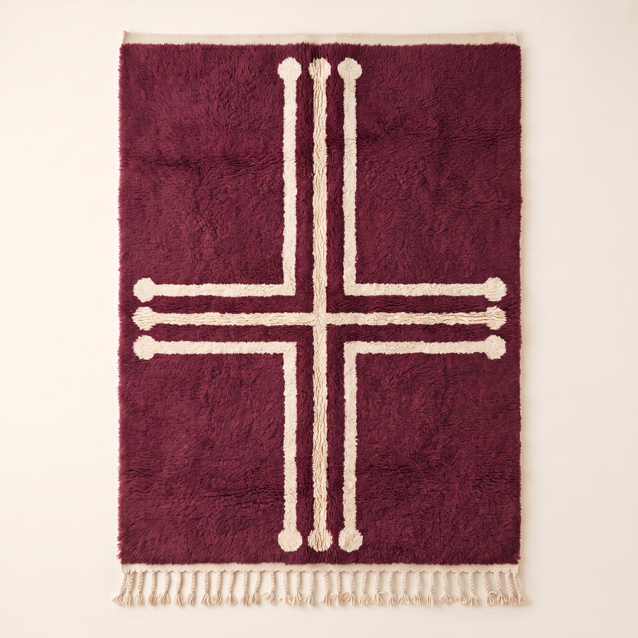 Plum and ivory Beni Ourain rug with bold geometric cross motif and decorative terminals, flat lay on plain background