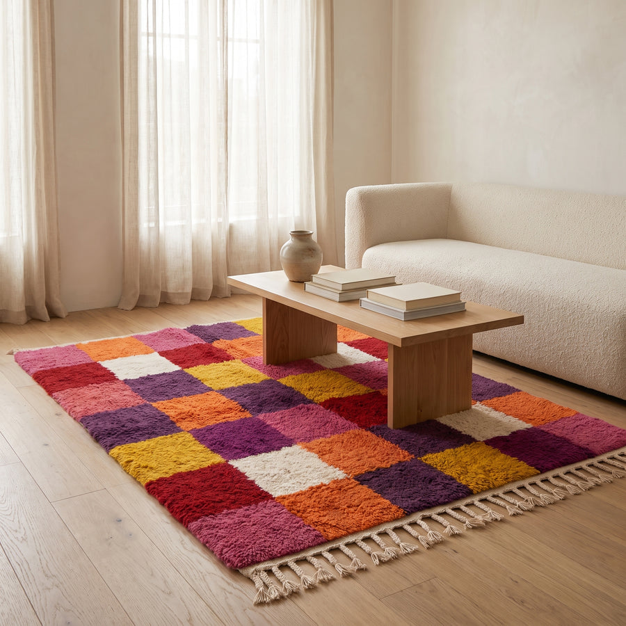 Red, orange, purple and gold Boujaad chequerboard rug in living room with cream sofa and wooden table