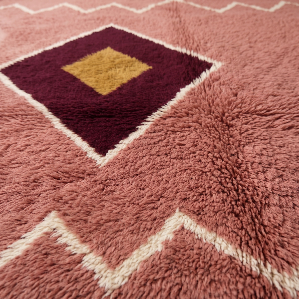 Close-up of diamond medallion showing thick wool pile with burgundy outer diamond, gold centre diamond, and cream outline detail