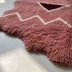 Edge detail of rose Beni Ourain rug showing thick wool fringe and irregular wavy border