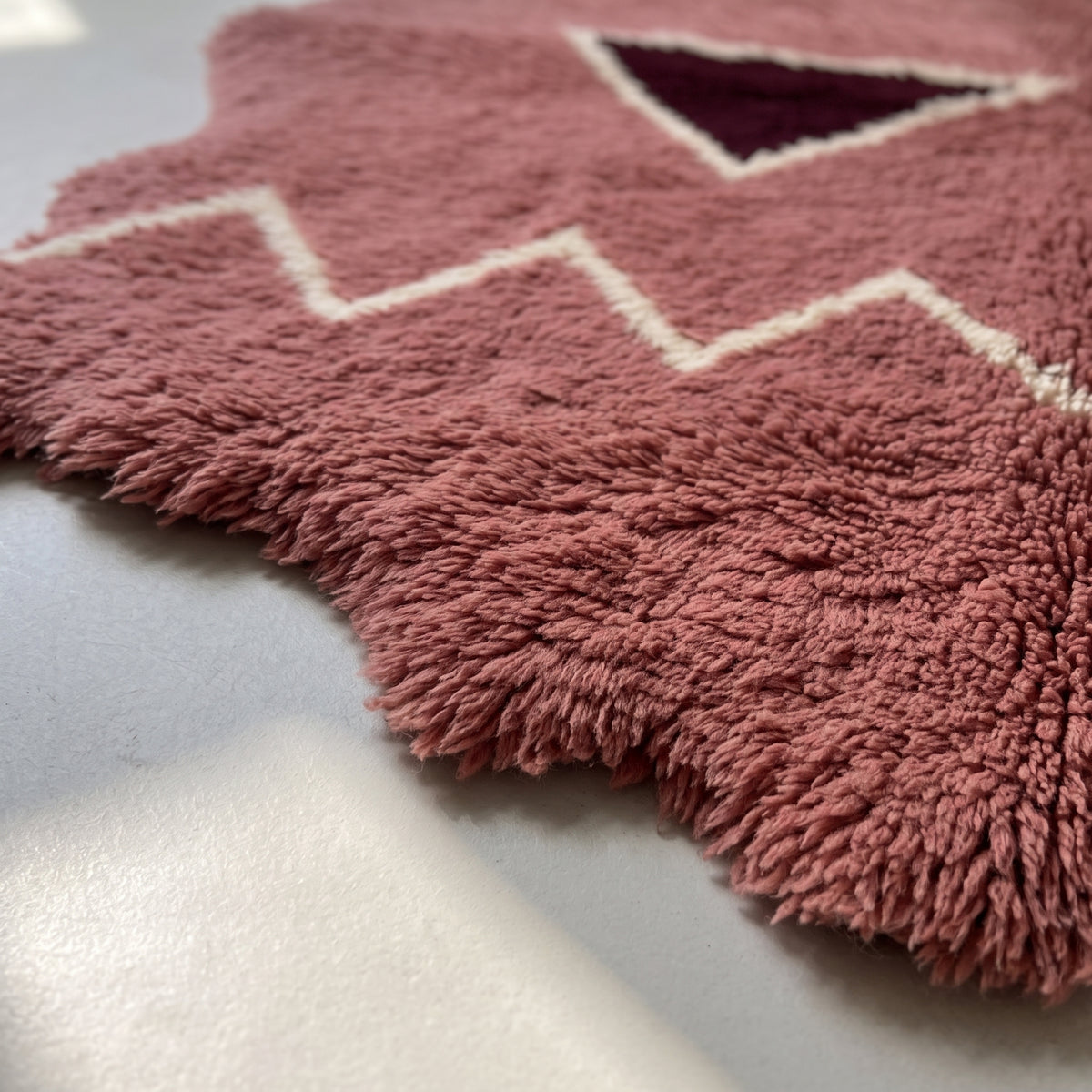 Edge detail of rose Beni Ourain rug showing thick wool fringe and irregular wavy border