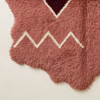 Bottom corner of rose Beni Ourain rug showing cream zigzag border pattern and irregular wavy edge