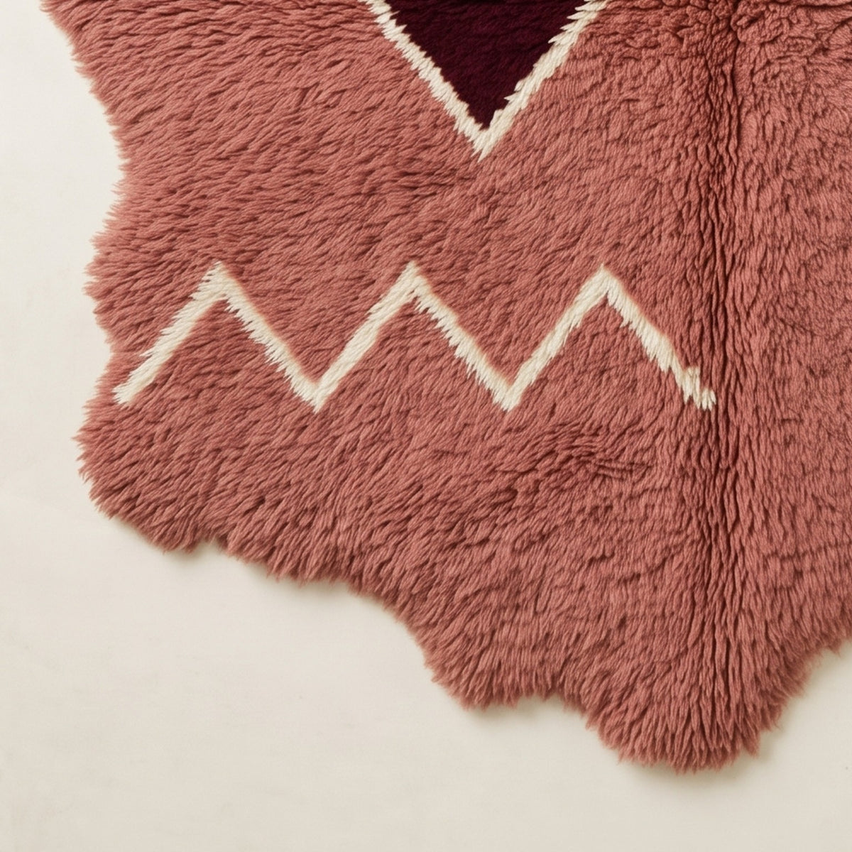 Bottom corner of rose Beni Ourain rug showing cream zigzag border pattern and irregular wavy edge